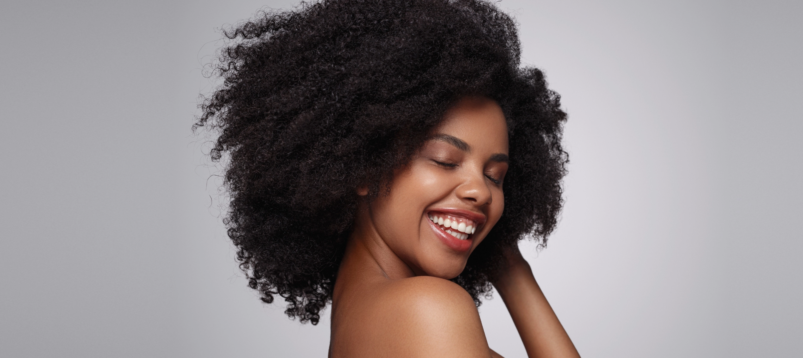 african american woman smiling with her eyes closed as her hand runs through her 4a type curly hair